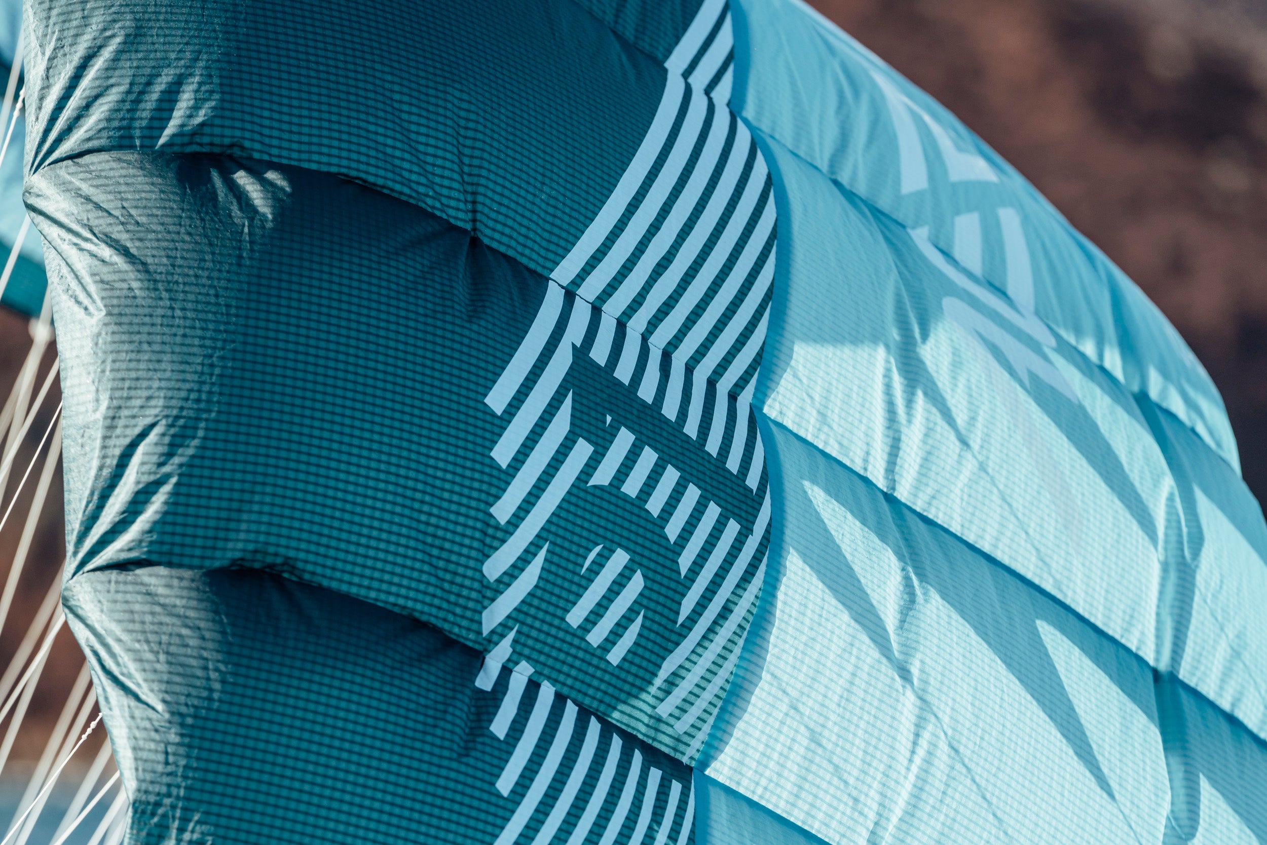 a close-up of the wing's fabric detailing. The turquoise Teijin material displays "AERYN" branding with striped graphic elements. The ripstop grid pattern is clearly visible, highlighting the lightweight yet durable construction that maintains shape during flight.