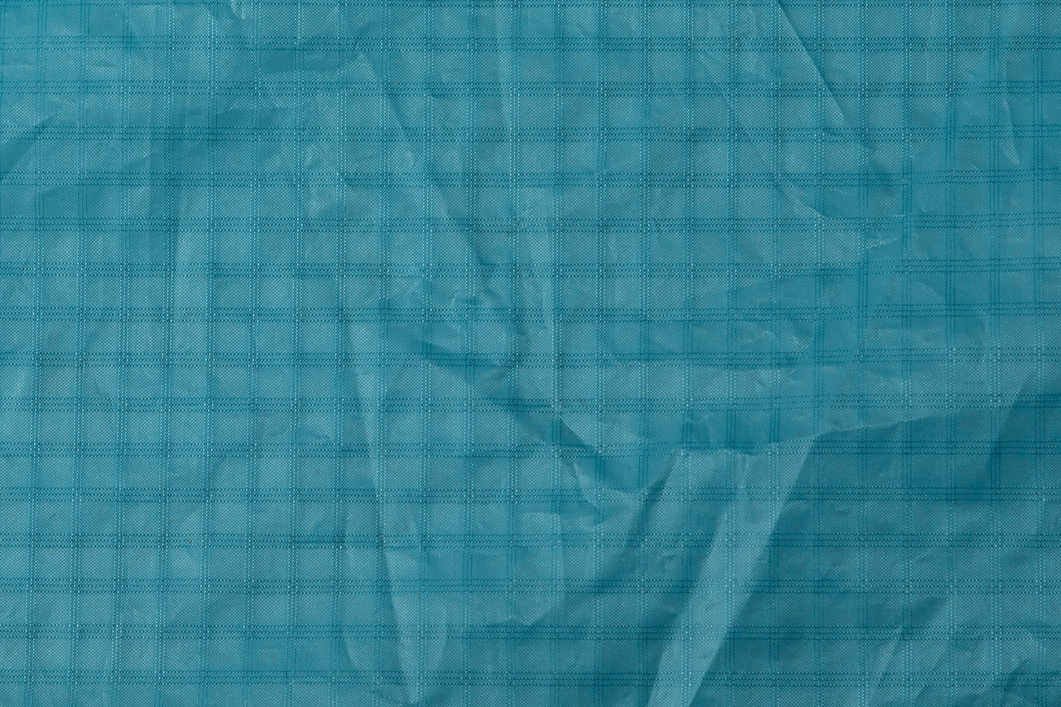 This is a close-up of the turquoise Teijin fabric used in the pocket wing parawing. The distinctive grid pattern is characteristic of Teijin's high-performance ripstop material, specially designed for wind sports equipment. The fabric's lightweight yet durable construction allows the pocket wing to maintain its aerodynamic shape while resisting tears and UV damage. The slight wrinkles and shadows visible in the material show the fabric's flexibility, essential for the dynamic inflation