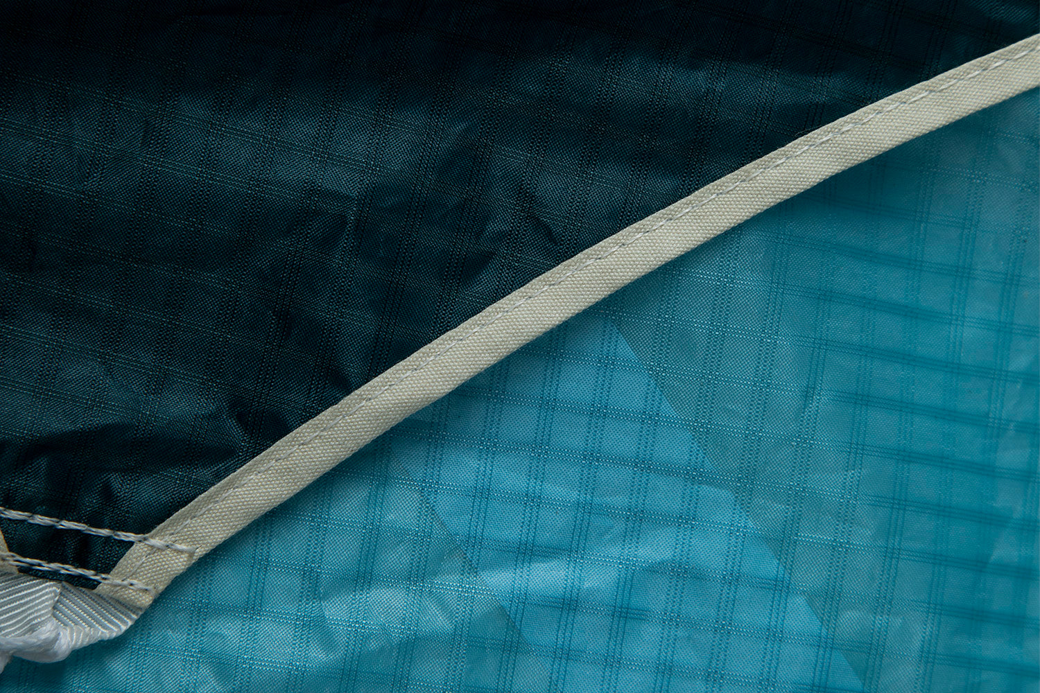 This image shows the color contrast and material transition in the pocket wing parawing. The turquoise Teijin fabric meets a darker navy/black section, with a cream-colored reinforcement tape running along the seam. The contrasting colors aren't just aesthetic—they serve functional purposes in the wing's design. The different panels work together to create the optimal aerodynamic profile, while the reinforced binding protects the edge from wear during inflation and handling.