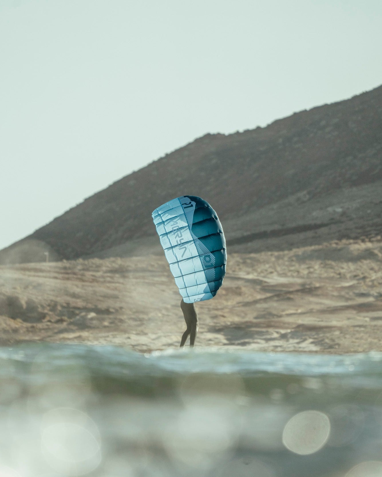 Person holding a blue parawing in a desert landscape with mountains in the background